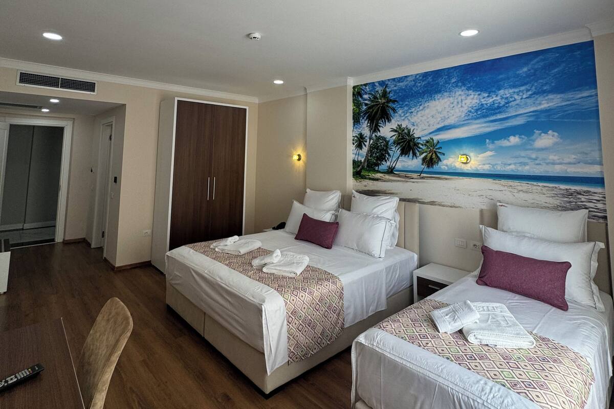 Quarto de hotel com duas camas, uma escrivaninha e uma cadeira. Há um quadro de uma praia na parede.