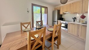 Une cuisine moderne avec des meubles en bois, un réfrigérateur en acier inoxydable et une table à manger pour quatre personnes.