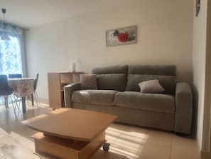 Ein Wohnzimmer mit Sofa, Couchtisch, Esstisch mit Stühlen und einem Wandbild.