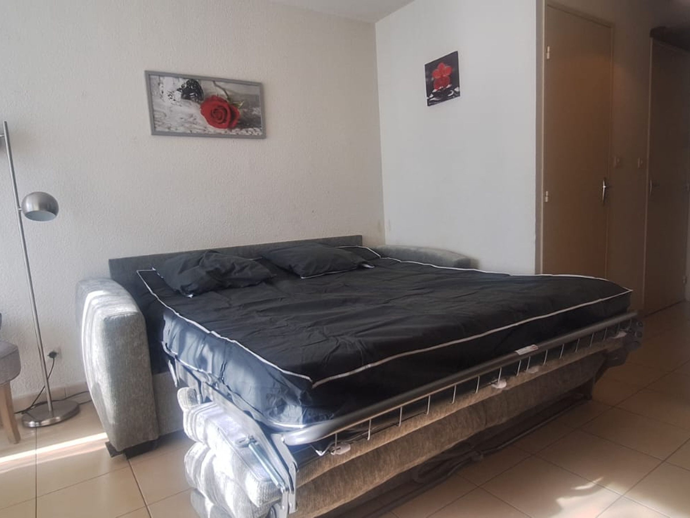 A bedroom with a bed, a wardrobe, a floor lamp, and two wall-mounted pictures.