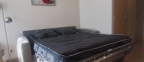 A bedroom with a bed, a wardrobe, a floor lamp, and two wall-mounted pictures.