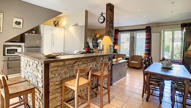 A kitchen with a stone island, wooden chairs, a dining table with chairs, a refrigerator, an oven, and a clock on the wall. - Charming F4 House, Terrace, 650m from Lamalou-les-Bains Thermes, Pet-Friendly (Lamalou-les-Bains)
