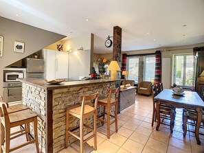 Een keuken met een stenen kookeiland, houten stoelen, een eettafel met stoelen, een koelkast, een oven en een klok aan de muur.