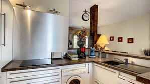 A modern kitchen with a built-in washing machine, a coffee maker, and a clock on the wall. - Charming F4 House, Terrace, 650m from Lamalou-les-Bains Thermes, Pet-Friendly (Lamalou-les-Bains)