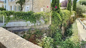 A stone building with white shutters, a garden with tall cypress trees, and a white fence. - Charming F4 House, Terrace, 650m from Lamalou-les-Bains Thermes, Pet-Friendly (Lamalou-les-Bains)