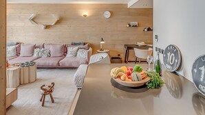 Een moderne woonkamer met een houten plafond, een roze bank, een eethoek met een fruitschaal en een wandklok.