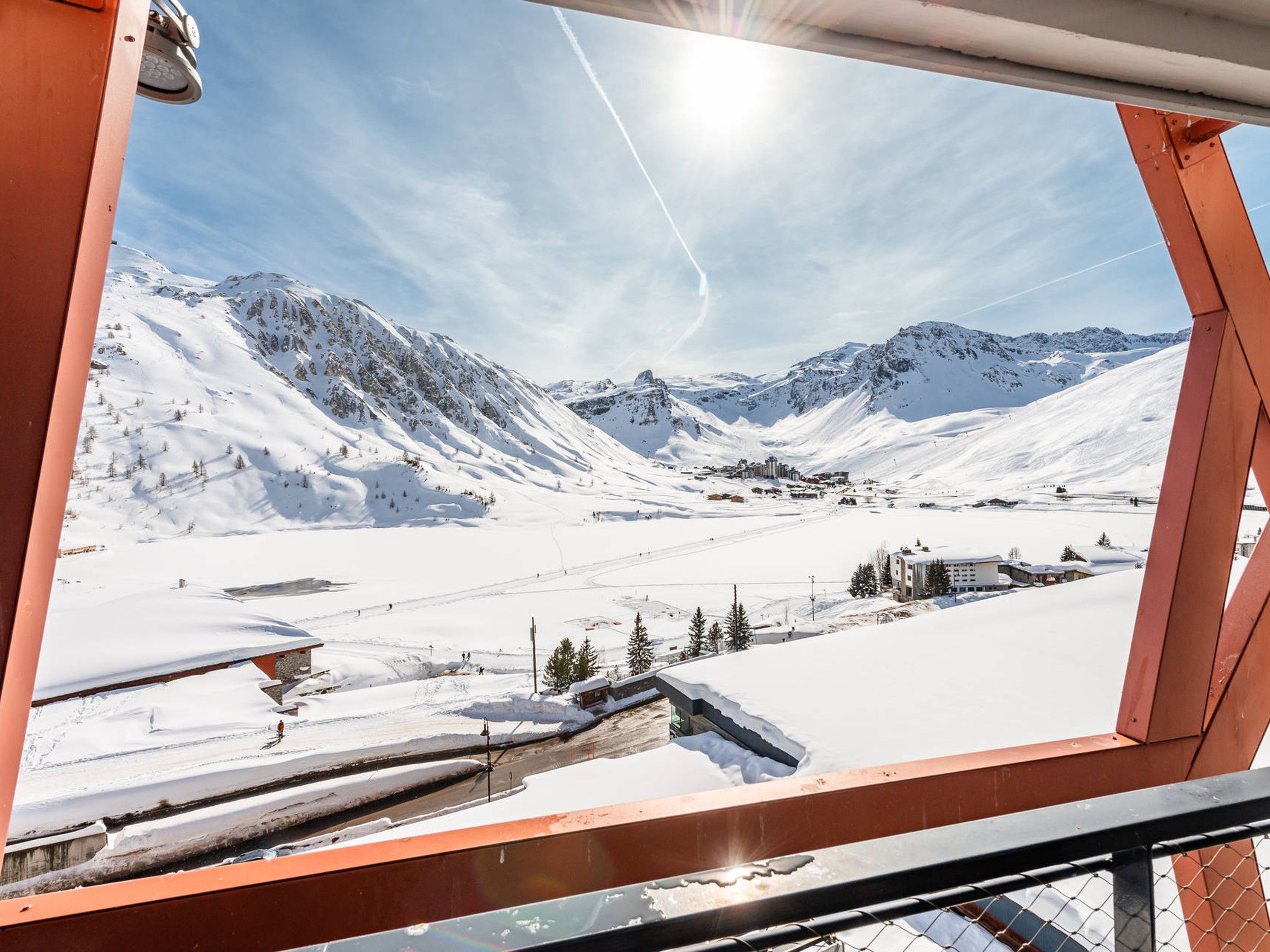 Une vue panoramique d’un paysage montagneux enneigé, avec un ciel dégagé, mettant en scène une station de ski avec ses bâtiments et ses pistes.