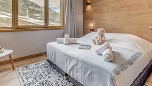 Een slaapkamer met een groot bed, een raam met uitzicht op een bergachtig landschap, een houten wand en een klein tafeltje met een teddybeer.