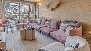 Een moderne woonkamer met een groot raam, een roze bank, een ronde witte stoel en een klein tafeltje met drankjes.