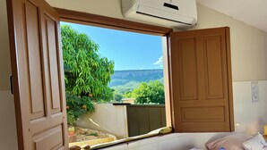 A bedroom with a large window, a bed with pillows, and an air conditioning unit.