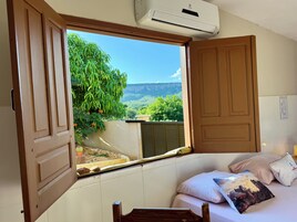 Un dormitorio con un ventanal grande, una cama con almohadas y un equipo de aire acondicionado.