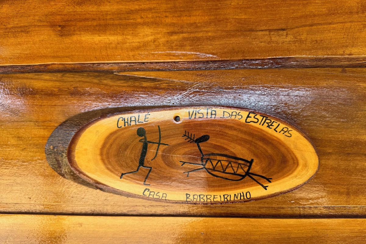 Een houten oppervlak met een gebeeldhouwde figuur van een rennende persoon en een boot, omringd door de tekst 'CHALE', 'VISTA DAS ESTRELAS', 'CASA' en 'BARREIRINHO'.