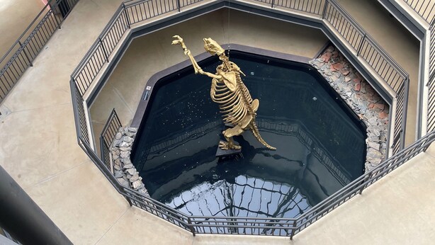 A multi-level atrium with a central water feature, including a golden statue of a creature, surrounded by a railing.