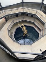 Un atrio de varios niveles con un elemento acuático central, que incluye una estatua dorada de una criatura, rodeado por una barandilla.