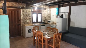 A compact kitchen with a stone wall, wooden beams, a washing machine, a microwave, and a refrigerator.