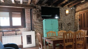 A rustic dining area with a stone wall, wooden ceiling beams, a fireplace, and a television mounted on the wall.