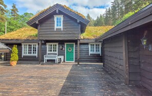A wooden cabin with a thatched roof, a green door, and a bench outside. - Nice home in Folkestad with sauna (Folkestad)