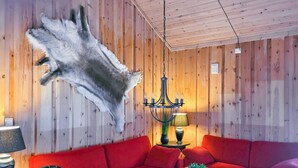 A room with a red sofa, a chandelier, and a mounted animal hide on the wall. - Nice home in Folkestad with sauna (Folkestad)