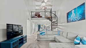 Un salon spacieux avec un grand téléviseur à écran plat, un canapé d’angle gris et un meuble de rangement bleu.