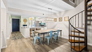 Une cuisine moderne avec un îlot central, un coin repas avec des chaises bleues et un escalier en colimaçon.