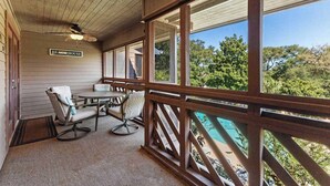 Une véranda abritée avec une table et des chaises, une enseigne indiquant « Maison de plage », et une vue sur une piscine.
