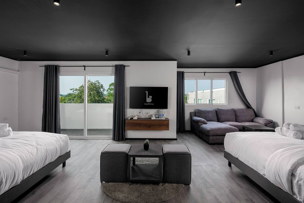 A modern bedroom with two beds, a sofa, a TV, and a sliding glass door to the outside.