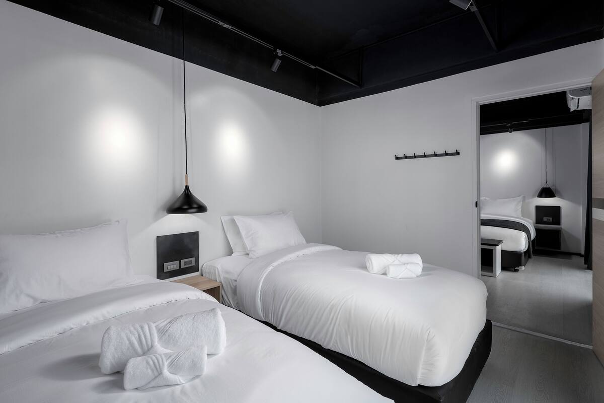 A modern hotel room with two beds, a bedside table, a lamp, and a mirror.