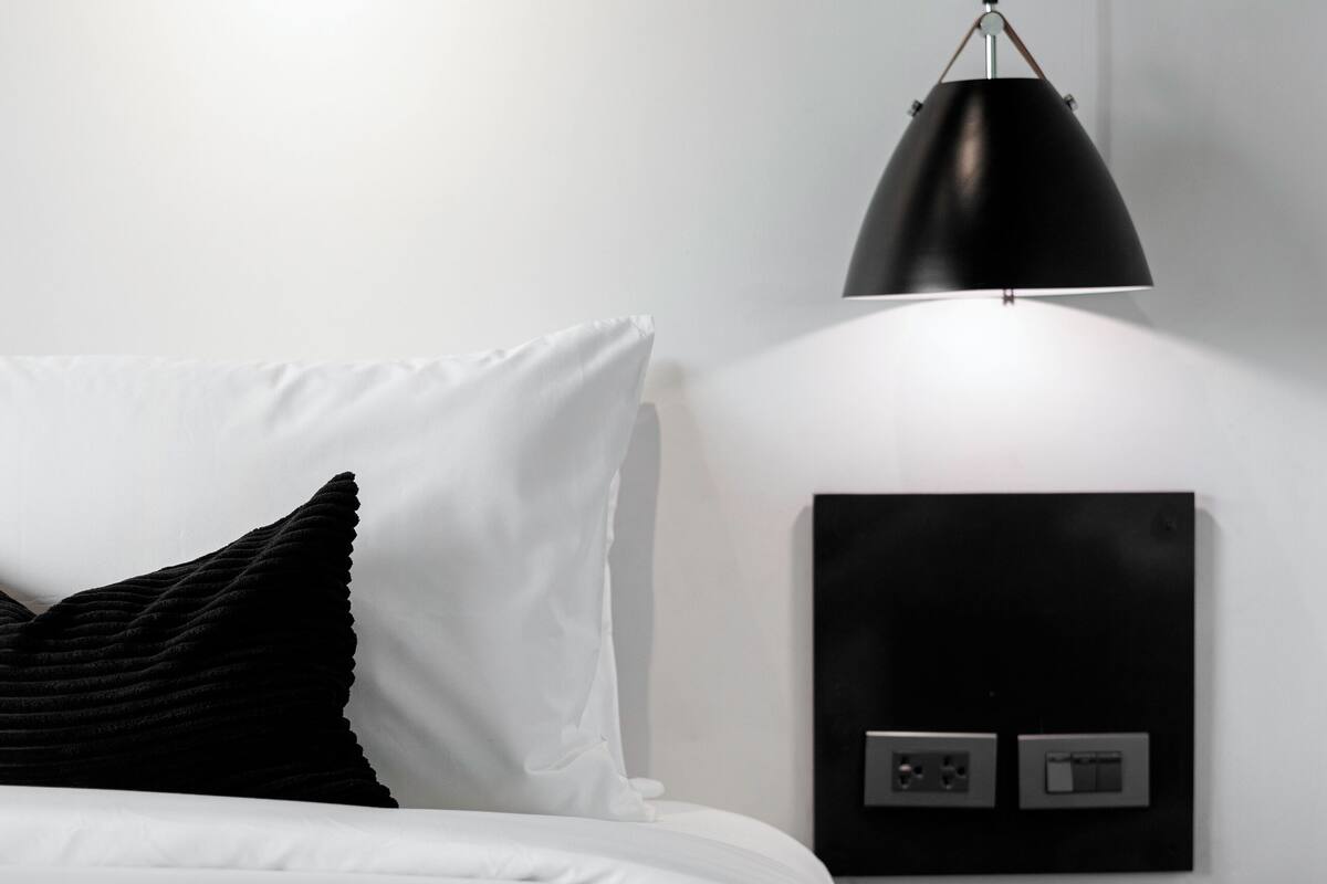 A modern bedroom with a bed, a black lamp, and a nightstand with a power outlet.