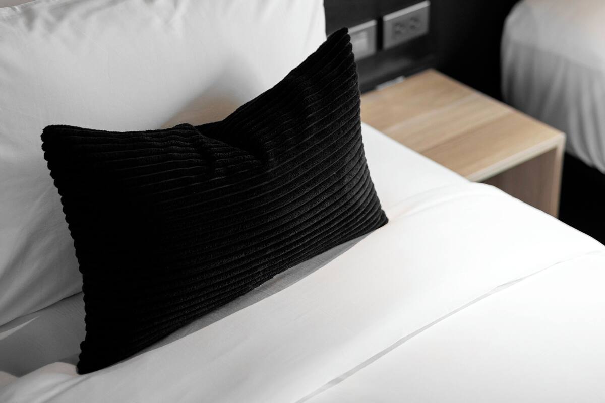 A bed with white and black pillows, a black lamp, and a wooden nightstand.