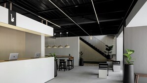 A modern reception area with a white counter, two laptops, a wooden table with stools, and a staircase in the background. - BedTime Hotel Samui (Koh Samui)