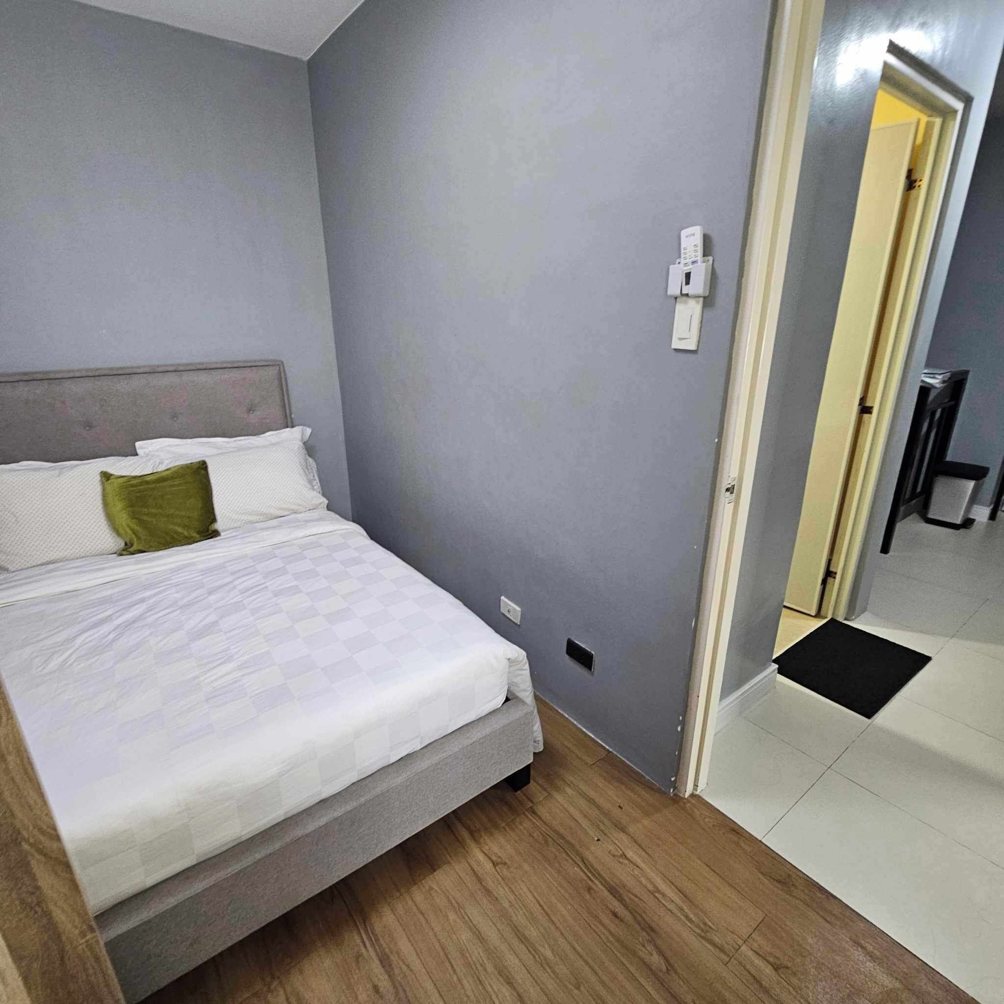 Un dormitorio con una cama, una pared gris y una puerta que da a otra habitación.