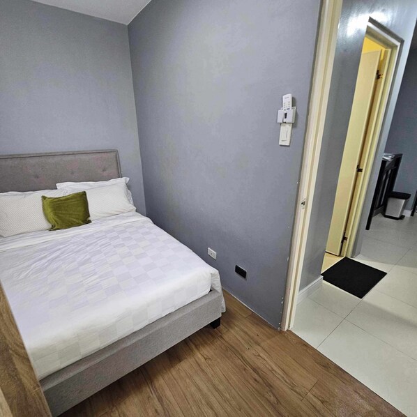 A bedroom with a bed, a grey wall, and a door leading to another room.