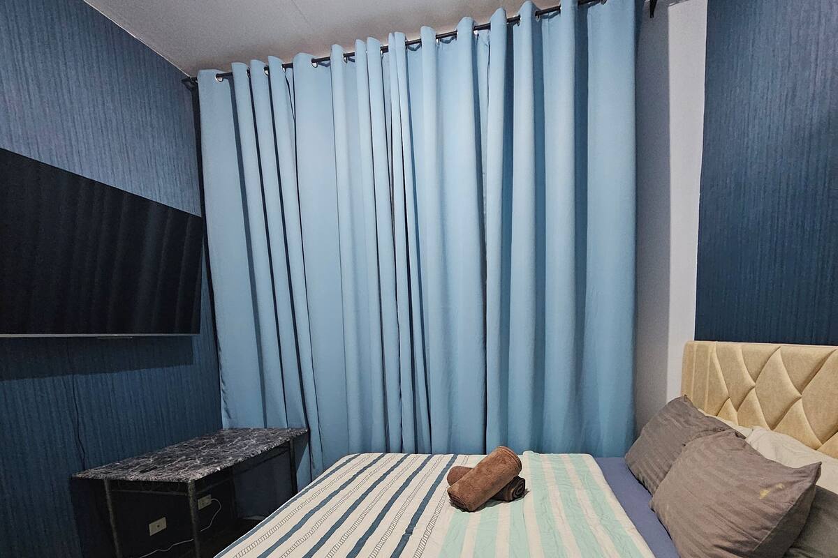 A bedroom with a bed, a TV mounted on the wall, and a small table.