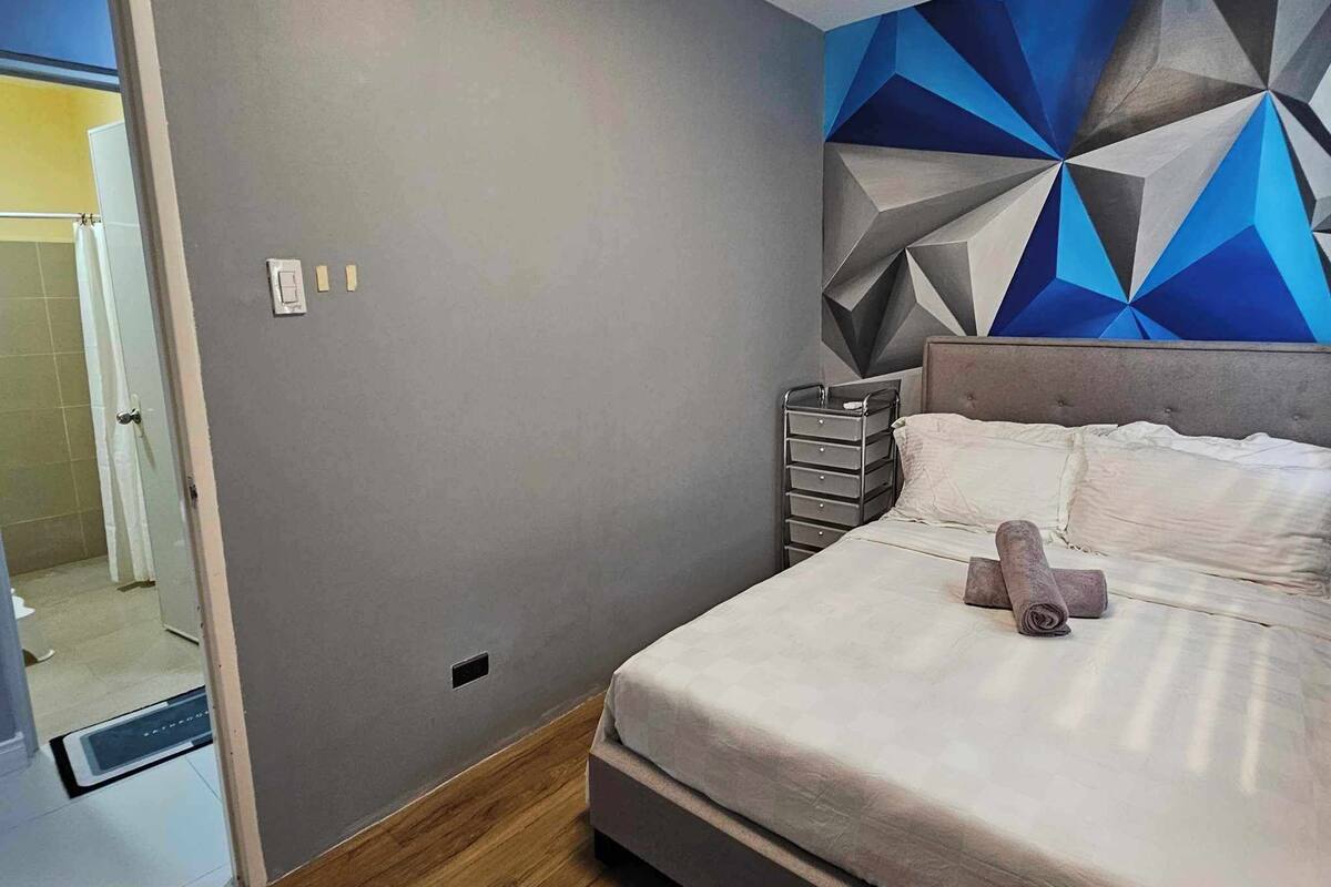 A modern bedroom with a geometric-patterned wall, a bed with white linens, and a wooden floor.