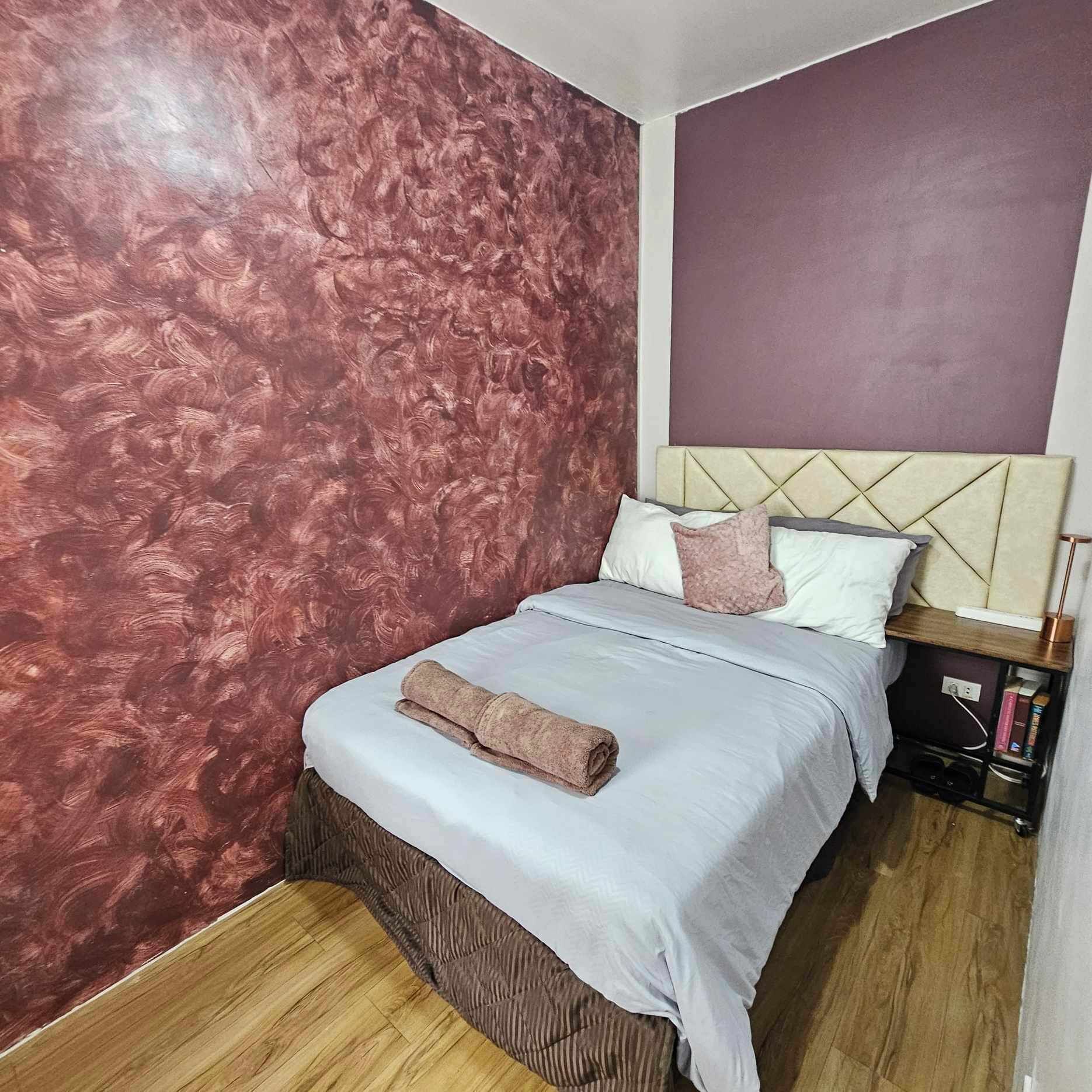 A bedroom with a bed, a nightstand, and a wall with a textured pattern.