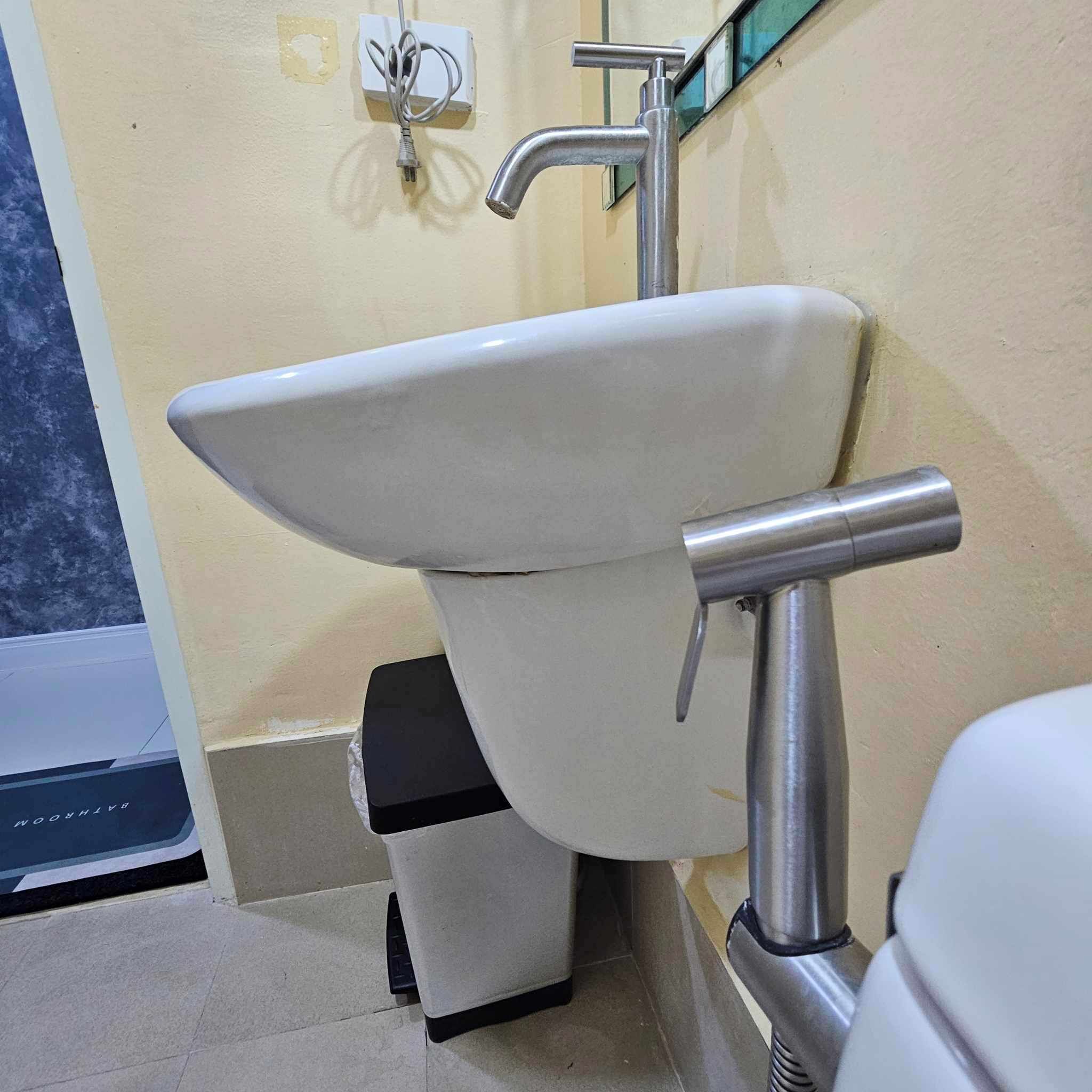 A bathroom with a white sink, a stainless steel faucet, and a trash bin.