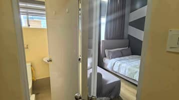 Ein Schlafzimmer mit einem Bett, einem Vorhangfenster, einem Deckenventilator und einer Tür zu einem Badezimmer.