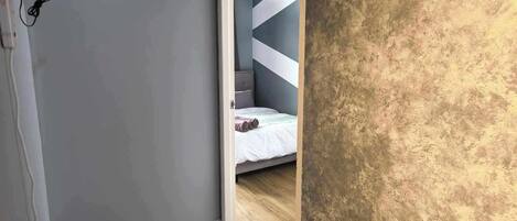 A bedroom with a grey wall, a wooden floor, and a bed with a white duvet.