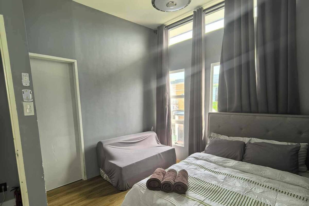 A hotel room with a large bed, a smaller bed, a window with curtains, a door, and a light fixture.