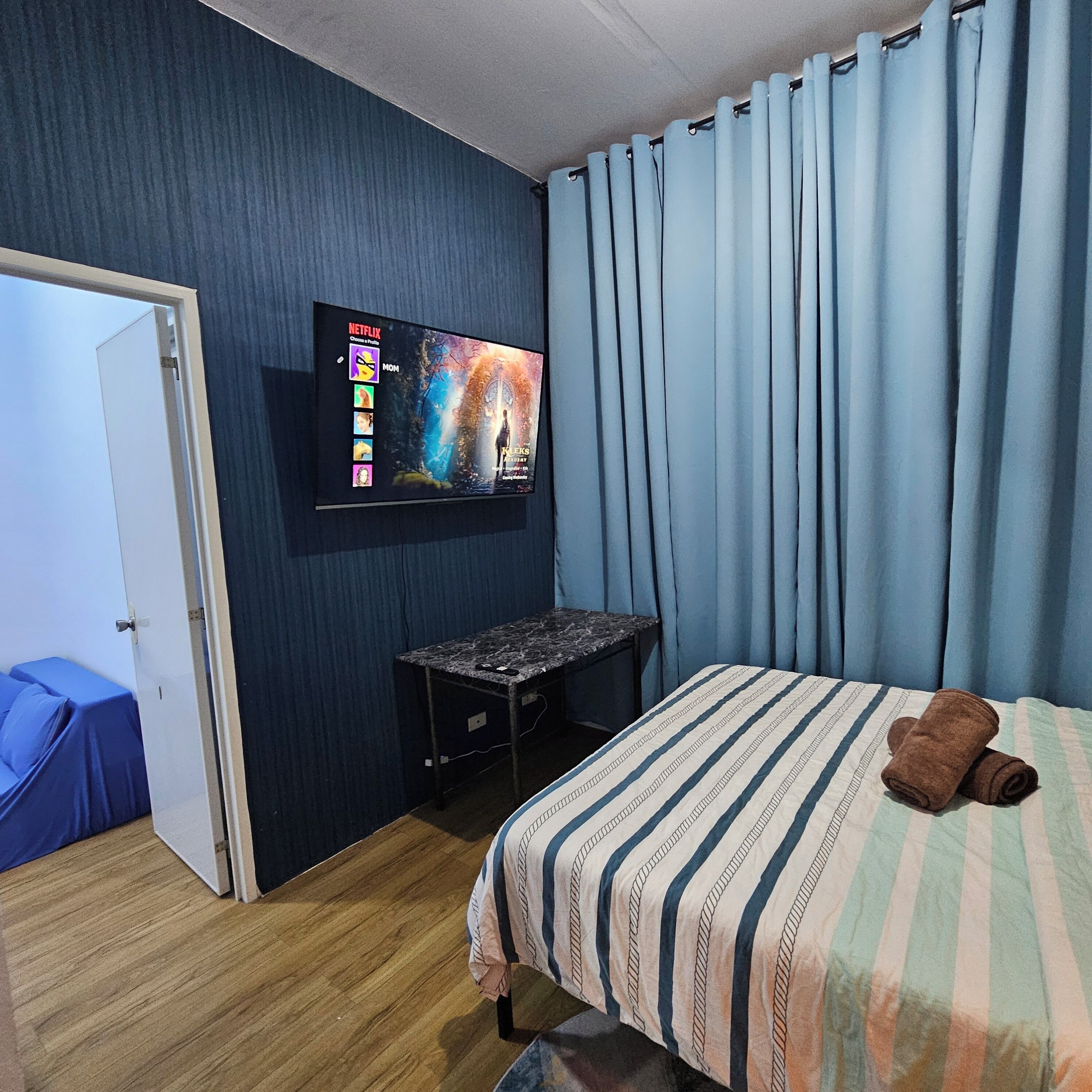 A hotel room with a bed, a desk, a TV mounted on the wall, and a door.