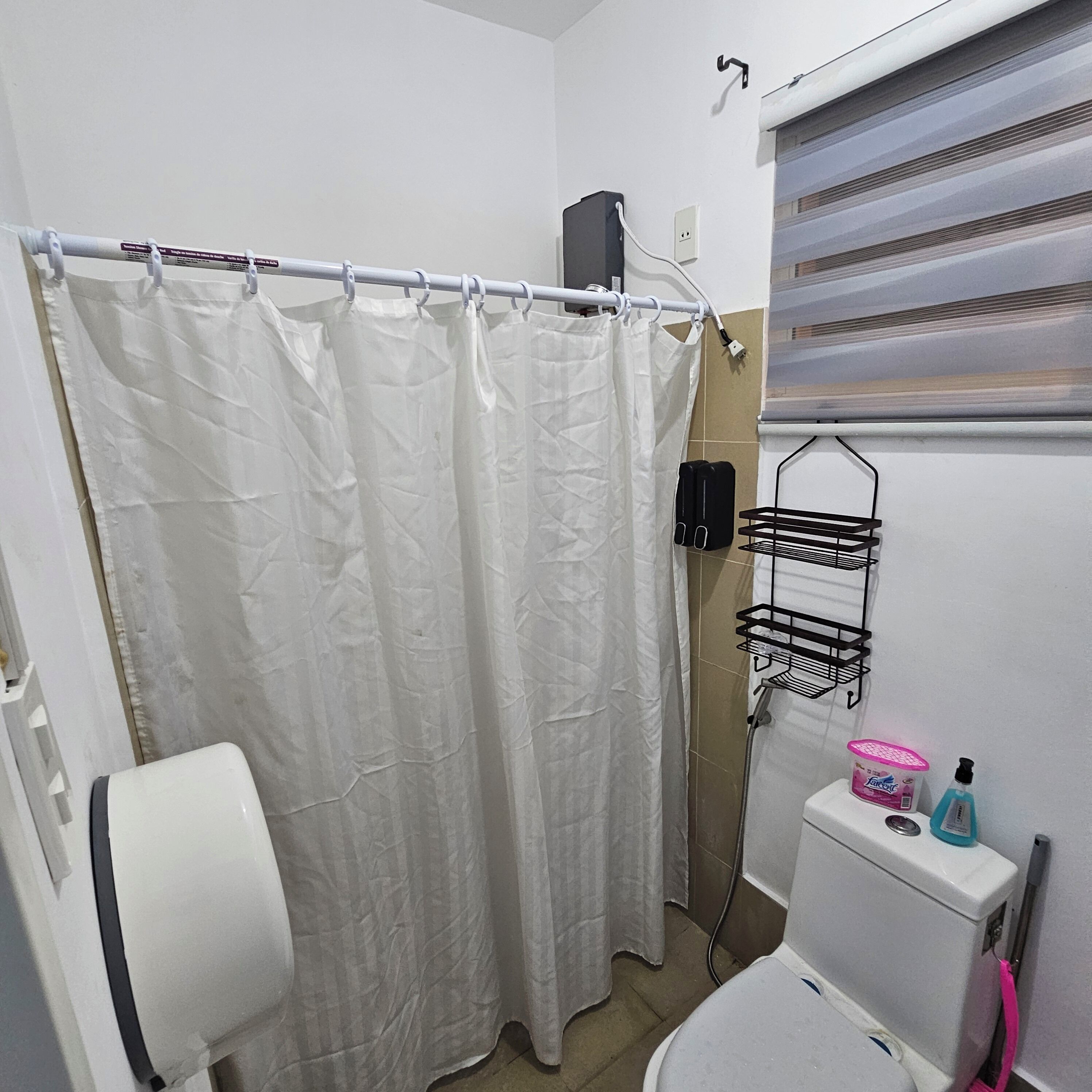 Un baño con cortina de ducha, inodoro, toallero y ventana con persianas.