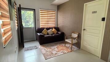 A living room with a dark brown leather sofa, a wooden chair, a patterned rug, and a door labeled 'E7'.