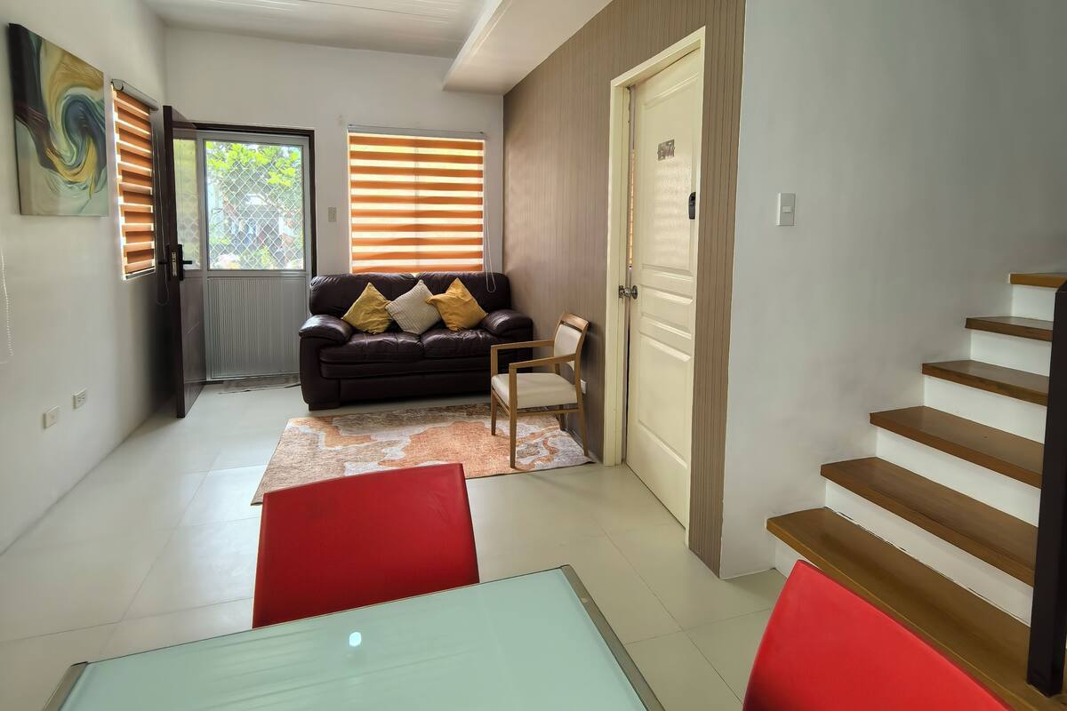 A modern living room with a sofa, a dining table, and a staircase.