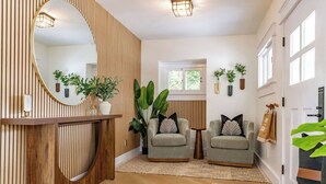 A modern living room with a wooden accent wall, two armchairs, a round mirror, and potted plants. - Stunning-5 Bed-Close To Zoo, Balboa Park, Downtown (San Diego)