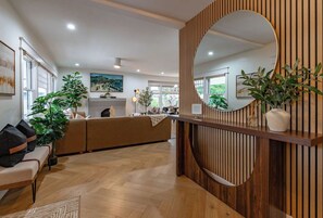 A modern reception area with a wooden reception desk, a large mirror, and a seating area with a sofa and chairs.