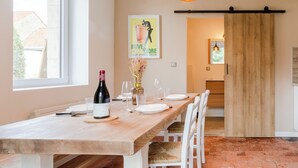 A dining area with a wooden table set for four, white chairs, a bottle of wine, and a poster on the wall.
