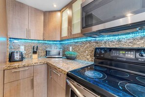A kitchen with wooden cabinets, a microwave, a toaster, a stove, and a backsplash with blue LED lighting. - Poolside Escape with Hot Tub Access | StayCozy (Miami)