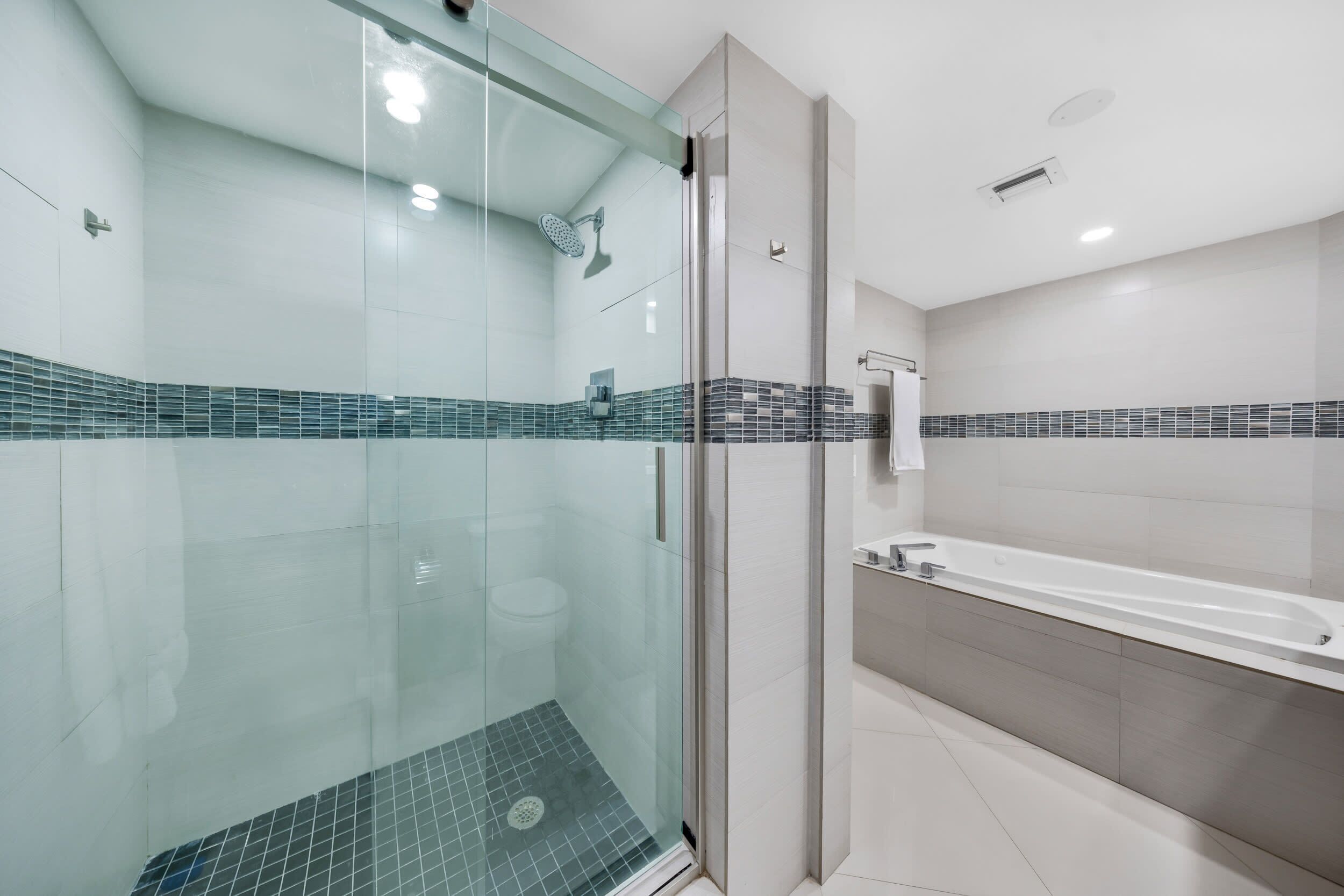 Une salle de bain moderne avec une douche à parois de verre, une baignoire blanche et un sol carrelé.
