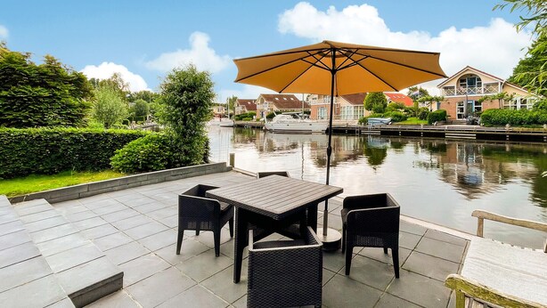 A patio with a table and chairs, a large umbrella, and a canal view. - 3 bedroom stunning home in Workum (Workum)