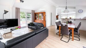 A modern living room with a black leather sofa, a dining table with chairs, a TV, and a wooden cabinet. - 3 bedroom stunning home in Workum (Workum)